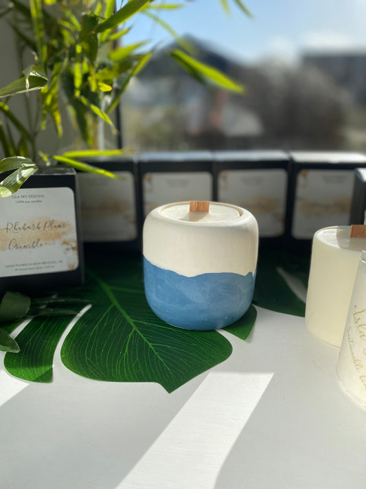 Rounded blue and white candle pot, approximately 10cm in height. Filled with a plant wax candle with a crackle wood wick. Along side are refills for the candle pot. 
